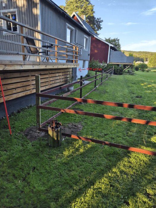 Trähus med altan och en ingärdad gräsmatta framför; ett staket har flyttats närmare garageporten, vilket nu hindrar användningen av garaget för fordon.