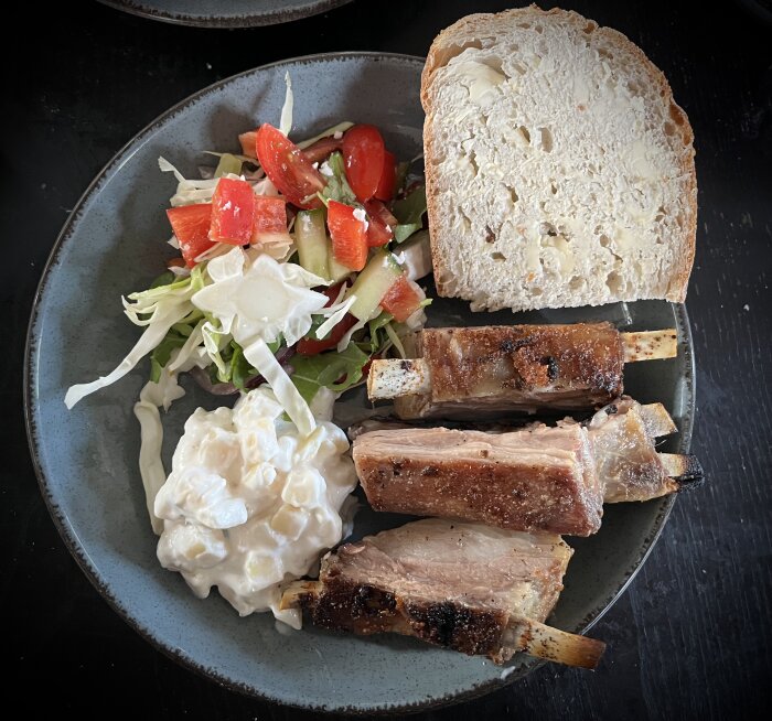 Tallrik med grillad fårbringa, skiva levainbröd, sallad med tomater och gurka, potatissallad.