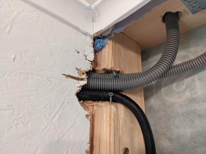Matningskabel och flexrör fixerade med gipsskruvar i en trasig vägg vid installation av undercentral och laddbox i ett garage.