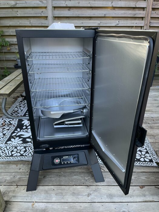 Masterbuilt 710 WiFi Digital Electric smoker with the door open, displaying the internal shelves and control panel on a deck with a patterned rug.