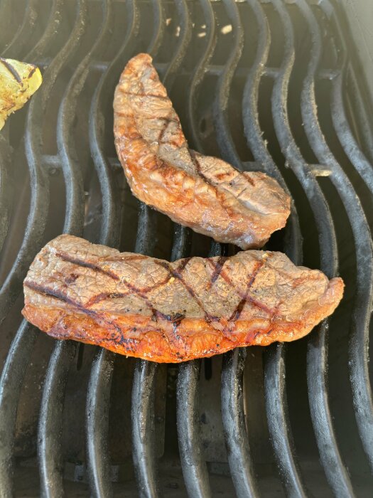 Två skivor grillad Picanha på en grill, med grillränder synliga på köttets yta. En liten bit av grillad zucchini syns också i hörnet.