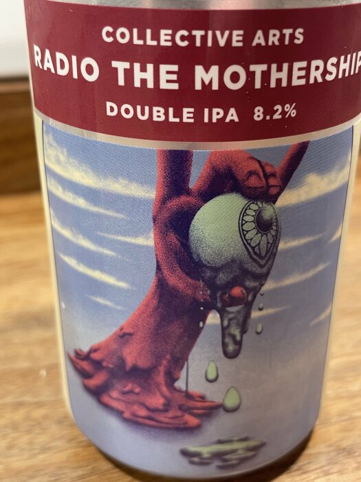 Ölburk med etikett som visar en surrealistisk bild av en hand som håller ett öga. Texten på etiketten lyder "Collective Arts Radio The Mothership Double IPA 8.2%".