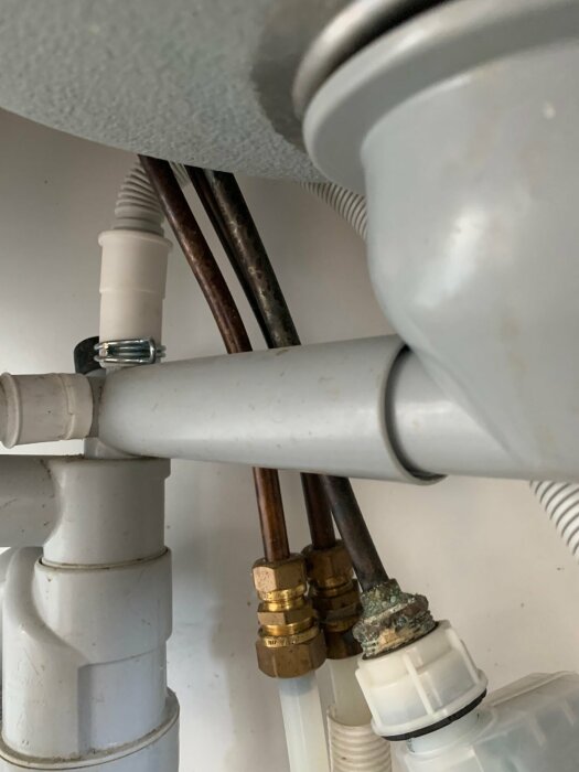 Närbild av VVS-rör och kopplingar under ett handfat, med både plast- och metallrör anslutna.