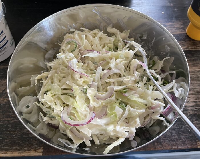 Skål med coleslaw innehållande strimlad vitkål, skivade padron och rödlök, blandat med en sås av gräddfil, fil, senap och svartpeppar.