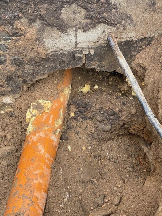 Avloppsrör i orange plast under jord och in till en mur som inte är gjuten, sett i ett dräneringsprojekt av en krypgrund.