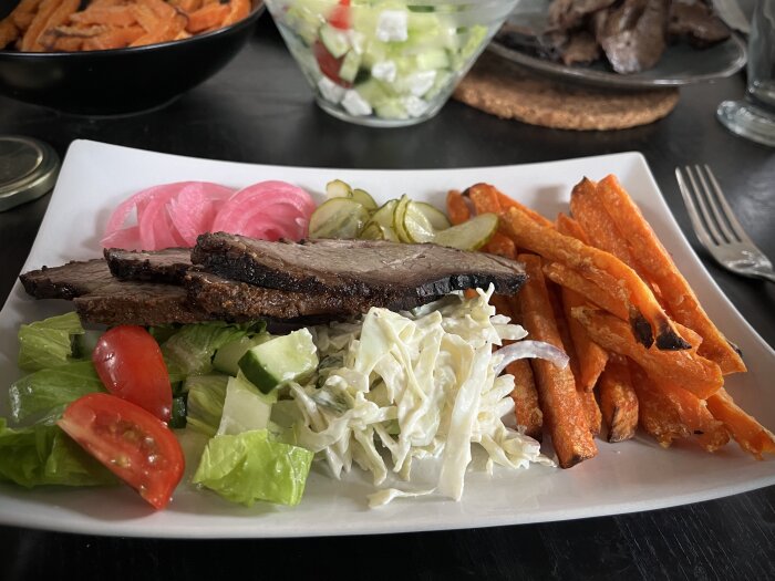 En tallrik med brisket, coleslaw, inlagd rödlök, inlagd gurka, sallad med tomat och gurka, samt sötpotatispommes.