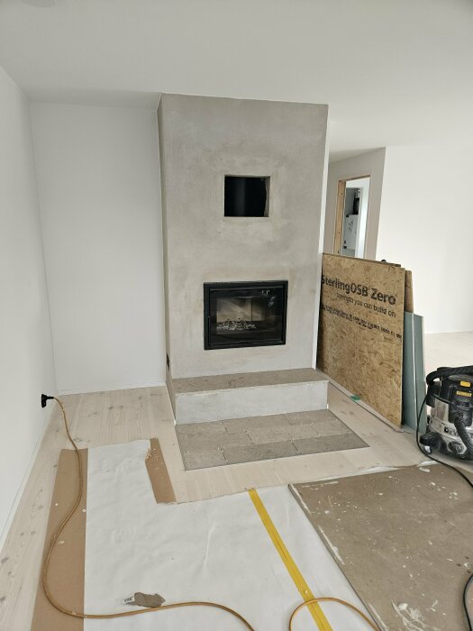 Renoverad murspis med insats och putsad yta i ett ljust rum, med skyddspapper på golvet och verktyg i närheten.