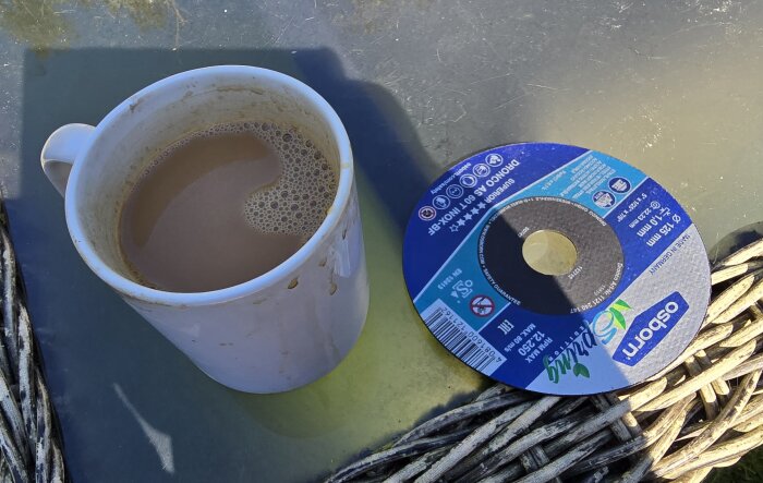 Kaffekopp bredvid en skiva från en vinkelslip ligger på ett glasbord.