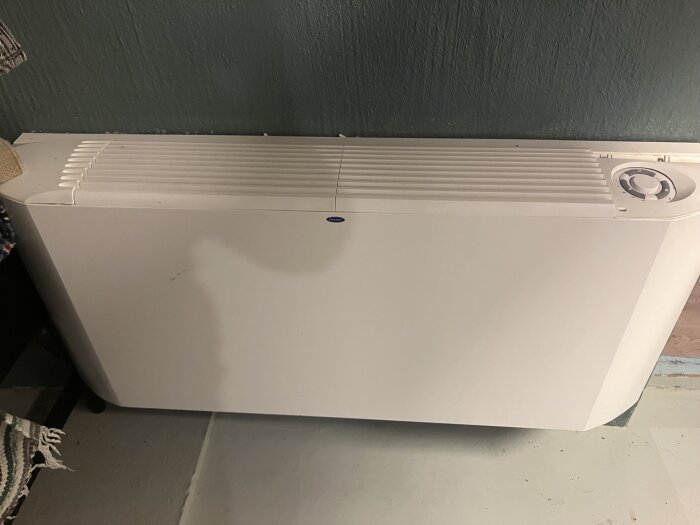 Vitt värmeelement i tvättstuga med galler och vred på överdelen.