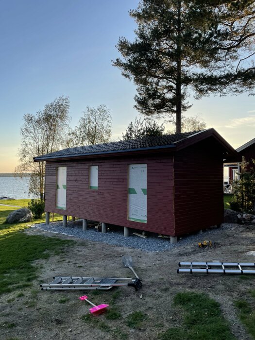 En nästan färdigmålad träbyggnad med täckta fönsteröppningar, omgiven av träd, ställningar och verktyg runt omkring.