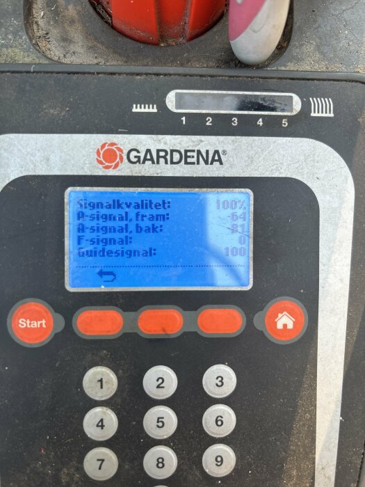 Närbild på en Gardena-enhet med en digital skärm som visar signalvärden för fram, bak och guide. Knappsatsen och startknappen syns också.