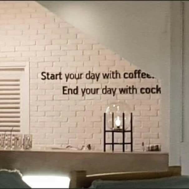 Vitt rum med en väggtext som säger "Start your day with coffee. End your day with cock". En lampa står på en hylla nedanför texten.