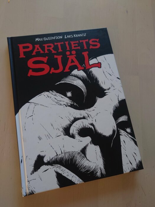 Framsida av seriealbumet "Partiets själ" av Max Gustafson och Lars Krantz, med en illustrerad teckning av ett ansikte i svartvitt och titeln i rött.