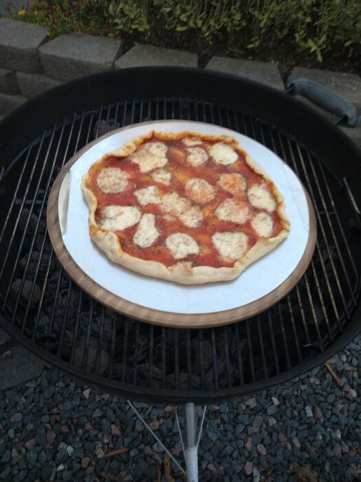 Pizza med chevre, päron och valnötter på en pizzasten i en grill.