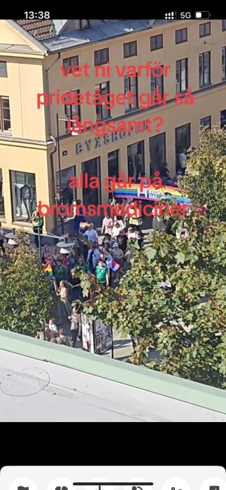 En Pride-parad rör sig långsamt genom en stadsgata. En byggnad med namnet "Byxshopen" syns i bakgrunden. Text på bilden: "vet ni varför pridètåget går så långsamt?