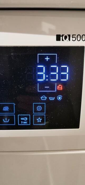 Närbild på digital display på en hushållsapparat, visande tiden 3:33 och en markerad röd symbol för avrinningsläge.