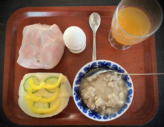 Frukostbricka med ägg, skinkskiva, ostsmörgås med gurka och paprika, havregrynsgröt samt ett glas äppelmust.