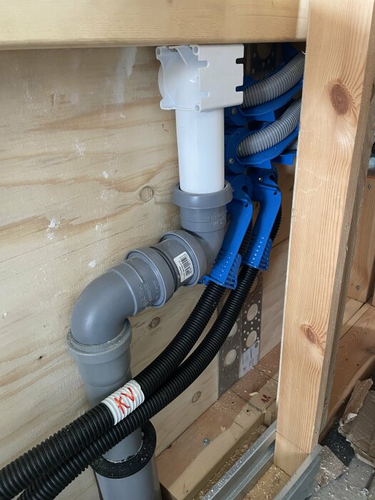 Installationssystem med pex-rör och vatette produkter, gråa och vita delar fixerade med blå bockningsfixturer, synliga bakom en öppnad vägg.