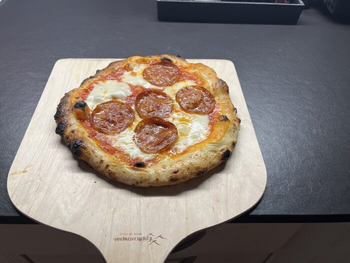 En nygräddad neapolitansk pizza med tomatsås, mozzarella och salami på en träspade.