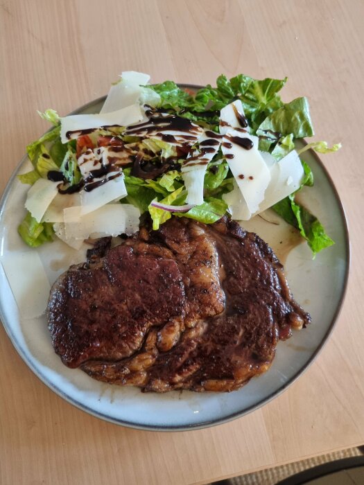 En tallrik med stekt entrecote och en grönsallad toppad med balsamvinäger och parmesanflingor.