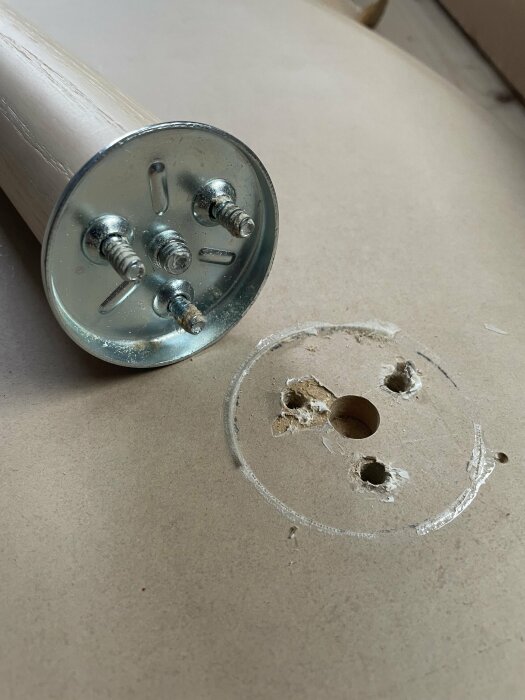 Löst bordsben med skruvar som lossnat från träskiva, och skadade hål i skivan där skruvarna har varit.