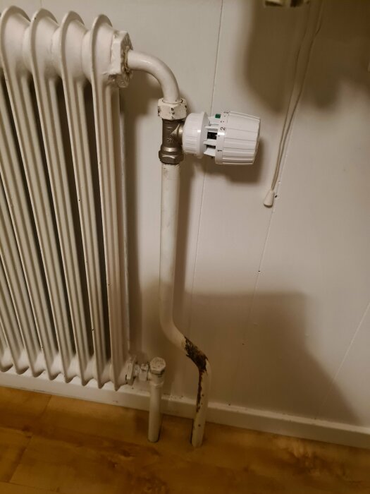 Vit värmeelement med nyinstallerad Danfoss termostatventil synlig i ett hus. Systemet är vattenburet och termostaten är graderad från 0 till 2.