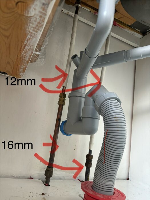 Rör under en diskbänk med markeringar, där ett rör har en diameter på 12mm och ett annat på 16mm, samt ett grått avloppsrör som löper snett nedåt.