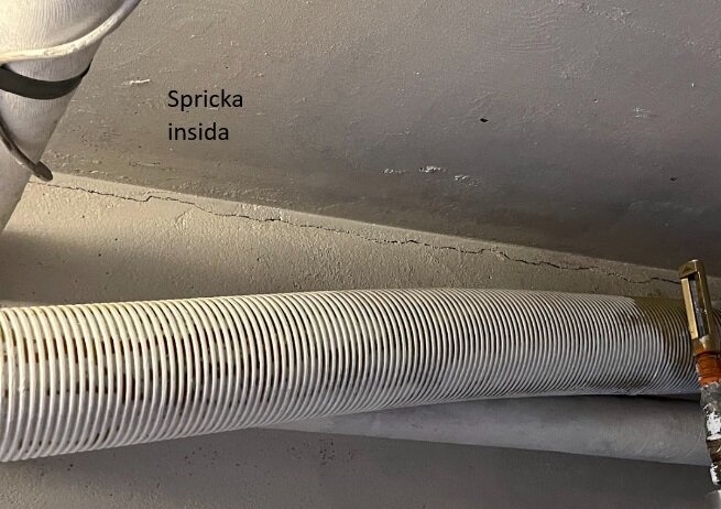 Horisontell spricka i ett betongbjälklag nära toppen av sockeln, med två rör parallelplacerade under sprickan. Texten "Spricka insida" är synlig på bilden.