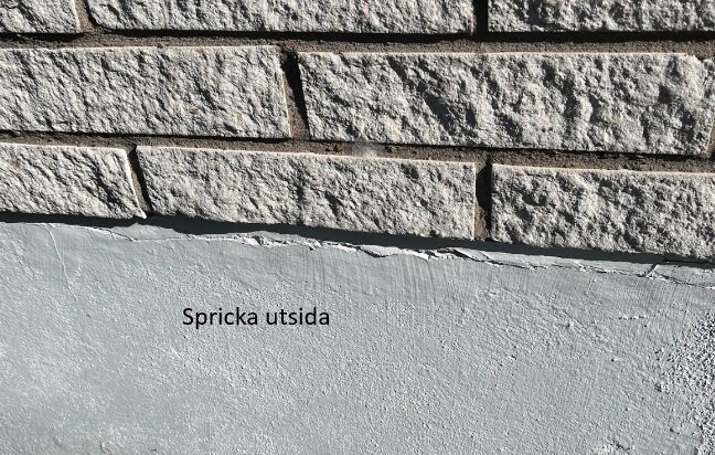 Horisontell spricka i sockeln på en villa, precis under den yttre tegelbeklädnaden. Texten "Spricka utsida" är synlig bredvid sprickan.