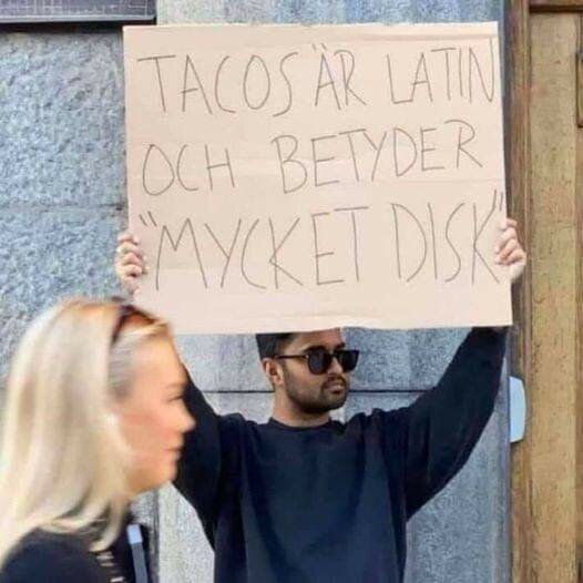 En person håller upp en skylt med texten "Tacos är latin och betyder 'mycket disk'".