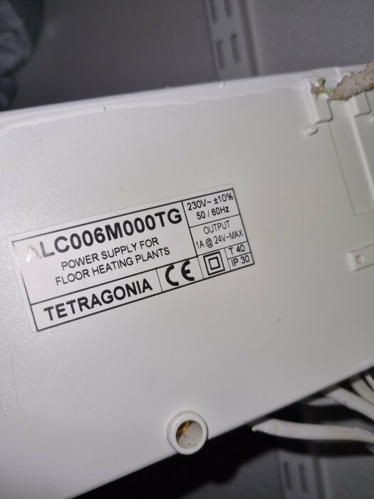 Kontrollenhetsskylt med text "ALC006M000TG" från Tetragonia, märkt för golvvärmeanläggningar med specifikationer 230V, 50/60Hz, 1A @ 24V-MAX, IP 30.