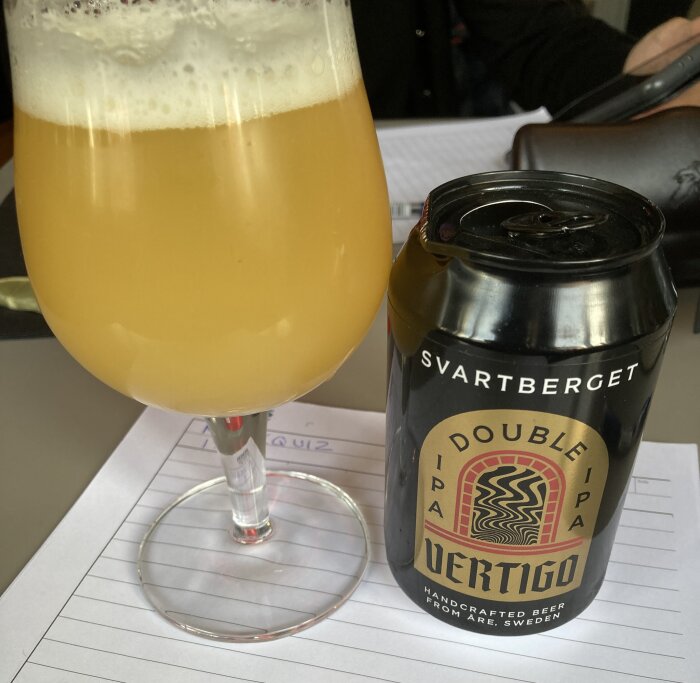 Ett glas skummande öl och en burk Svartberget Double IPA Vertigo står på ett anteckningsblock inför ett musikquiz.