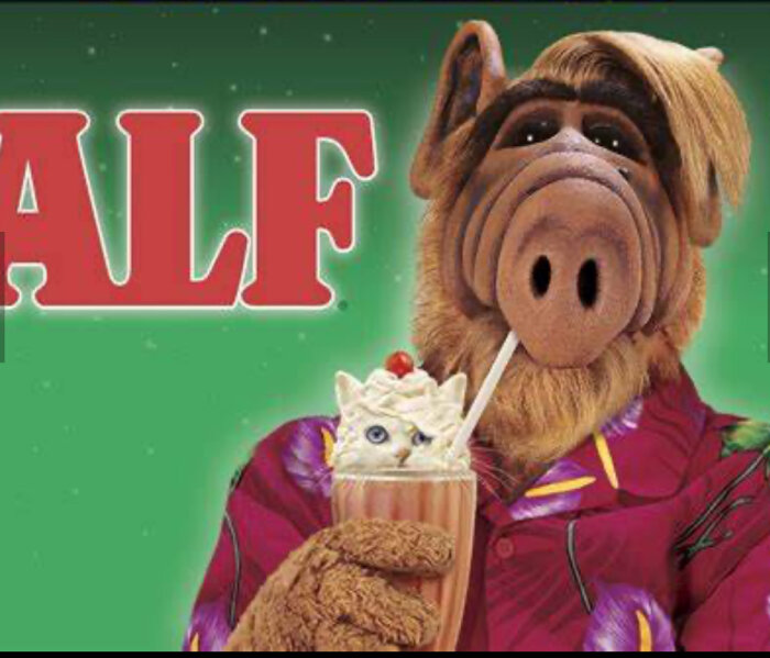 ALF i en färgglad skjorta dricker en milkshake med vispgrädde och katt i glaset.