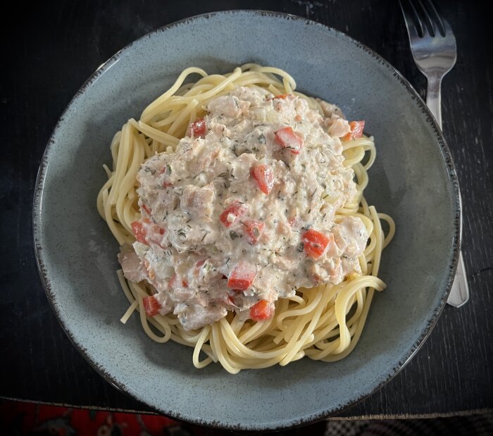 Tallrik med spagetti toppad med en krämig pastasås innehållande rökt lax, lök, paprika, dill, persilja, citron, matlagningsgrädde och fetaost.