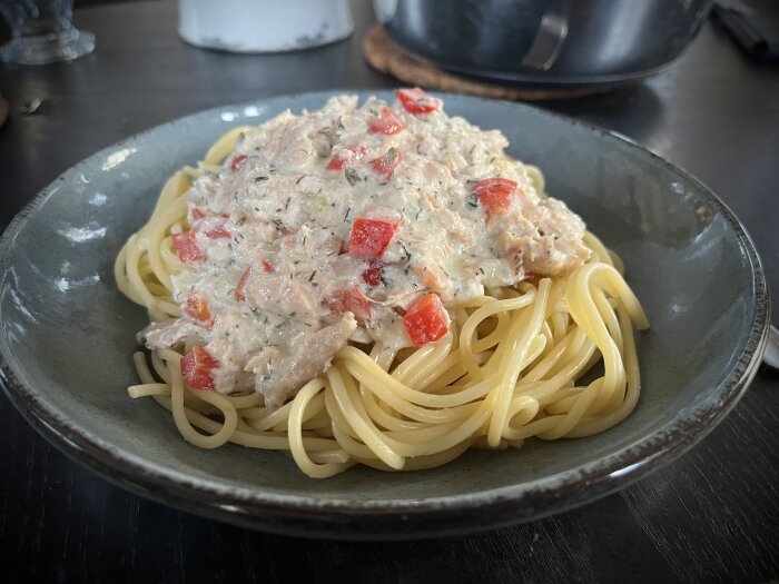 Tallrik med spagetti toppad med en krämig pastasås innehållande rökt lax, lök, paprika, dill, persilja, citron, matlagningsgrädde och fetaost.