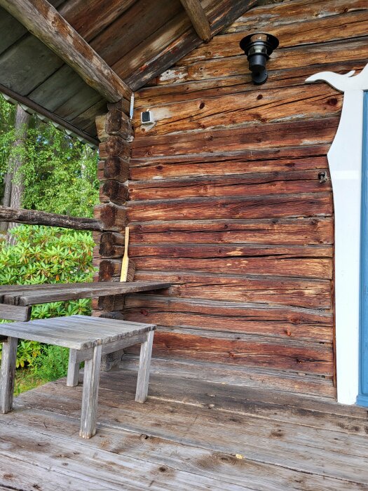 En vägg av en gammal lada på en fäbod, med utomhusbelysning, ett träbord och en bänk. Väggen är solblekt och har en naturlig patina.