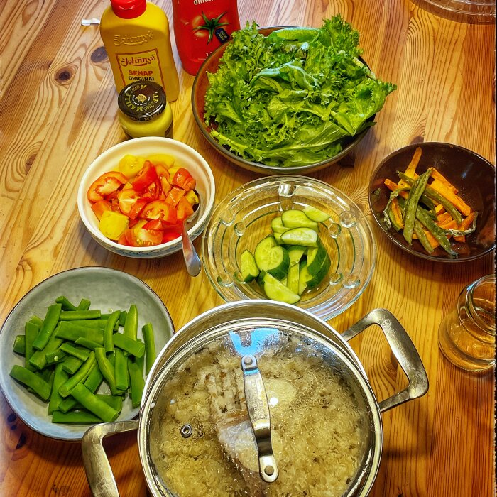 Bordsdukning med sallad, stuvade makaroner i en kastrull och olika grönsaker inklusive tomater, ärtor och gurka. Johnny's senap och ketchup syns i bakgrunden.