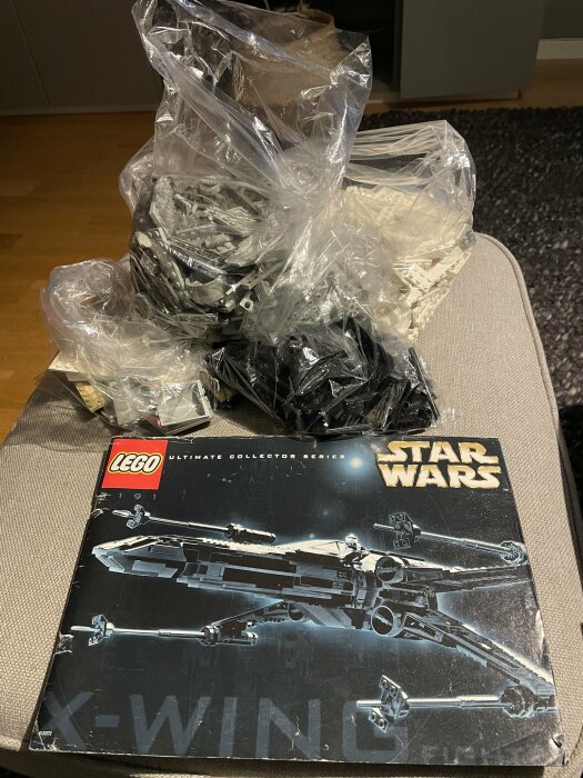 Lego Star Wars Ultimate Collector Series X-Wing-set med plastpåsar fyllda med klossar på en soffa.