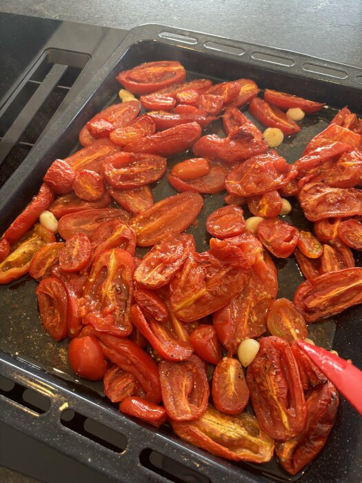 Rostade San Marzano-tomater och vitlöksklyftor på en ugnsplåt, förberedda för att bli tomatsås till pizza.