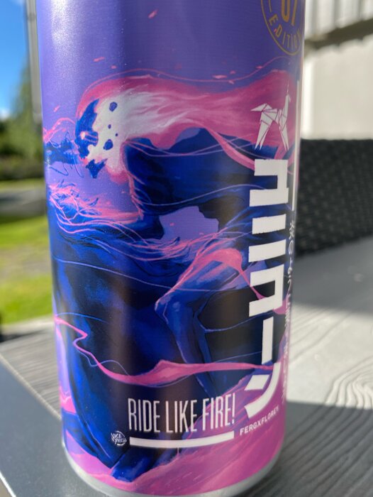 Närbild på en ölburk med etiketten "Ride Like Fire!" från Rivington Brewing Co, med färgstarkt grafiskt tryck i lila och blå toner.