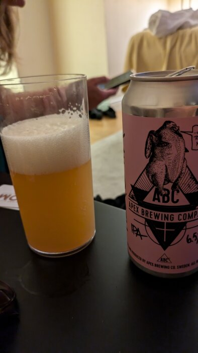 En burk med Apex Brewing Company IPA och ett glas med skummande öl på ett bord.