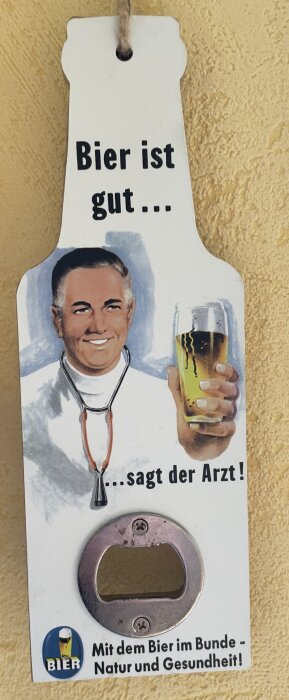 Bild av en flaskformad ölöppnare med en illustration av en läkare som håller en öl och texten "Bier ist gut... sagt der Arzt!" och "Mit dem Bier im Bunde - Natur und Gesundheit!".