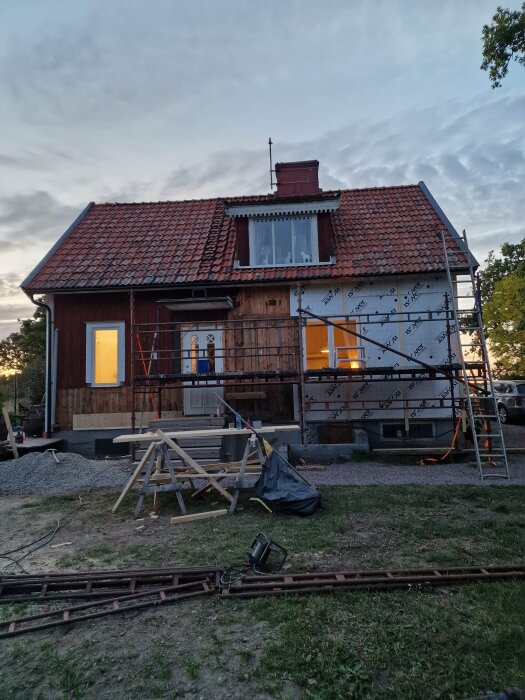 Ett hus under renovering med ställningar och byggmaterial runt omkring, en del av huset har fått ny isolering.