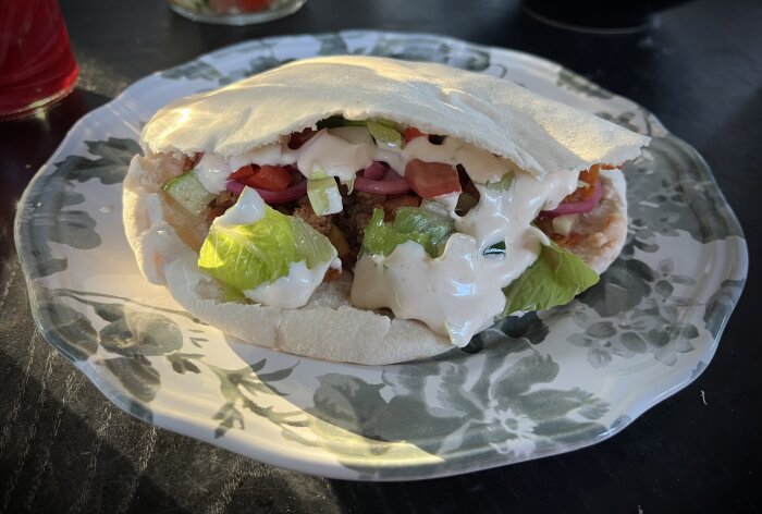 Chili con carne i pitabröd toppat med sallad, picklad rödlök och sås, serverat på en blommönstrad tallrik.