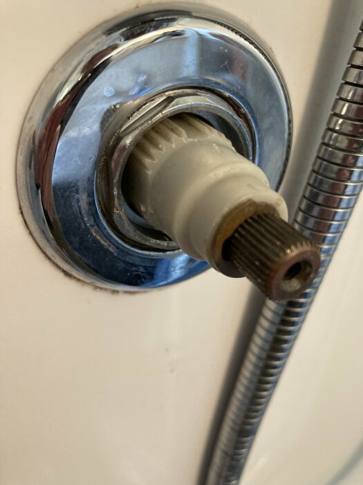 Närbild på termostat i en ångdusch, med synlig mutter och anslutande metallslang, som användaren försöker lossa.