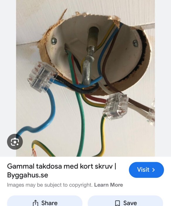 Gammal takdosa i ett äldre hus med ojordade, färgade elledningar som hänger ned, temporärt installerad taklampa, visar sladdar och anslutningar.