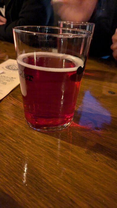 Ett glas rödaktig dryck på ett träbord, troligtvis "Ramunders Mjöd", som enligt inlägget smakar mer som cider än honung.