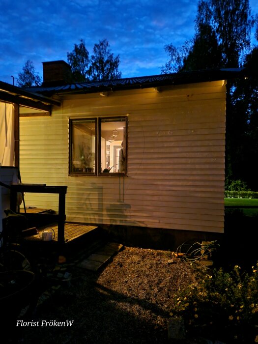 En väg med träpanel och fönster på ett hus, tagen på kvällen med utomhusbelysning.