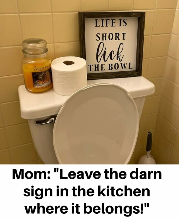 En skylt med texten "LIFE IS SHORT lick THE BOWL" står på en toalett, bredvid en toalettrulle och ett doftljus. Texten nedanför bilden säger: "Mom: Leave the darn sign in the kitchen where it belongs!