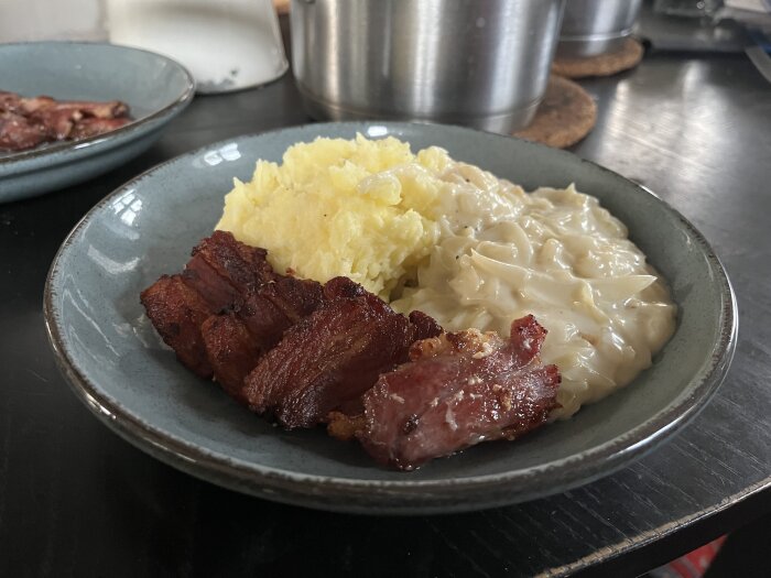 En tallrik med stekt fläsk, potatismos och vitkålssås på ett bord i ett kök.